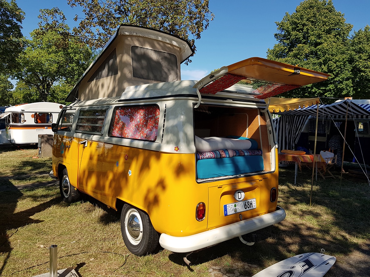 Gelber VW Bus Oldtimer Camper mit aufgestelltem Dach auf dem Campinggelände