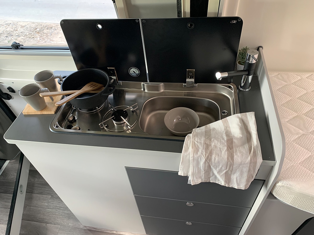 Küche im Ahorn Camp Van 620 Black Edition mit hochklappbarer, zweiteiliger Arbeitsfläche, Spülbecken und Zweiflammenkocher