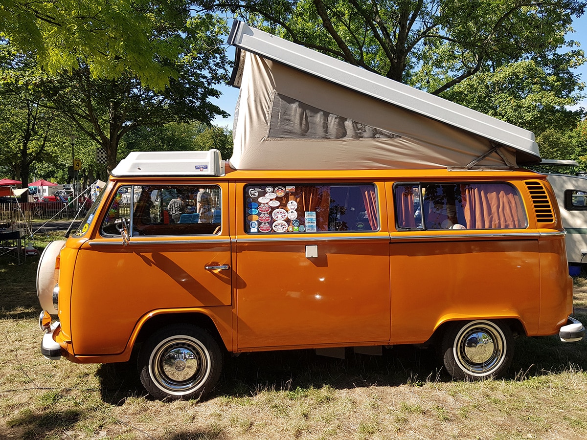 Orangefarbener VW T2 Campingbus mit Aufstelldach und Reiseaufklebern