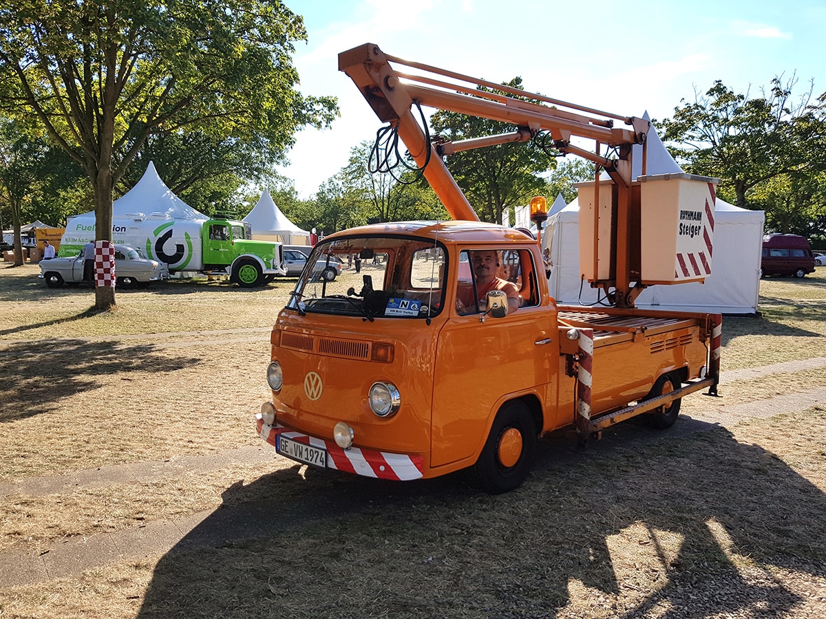Orangefarbener VW T 2 Pritschenwagen mit Hebebühne in Fahrt über das Gelände
