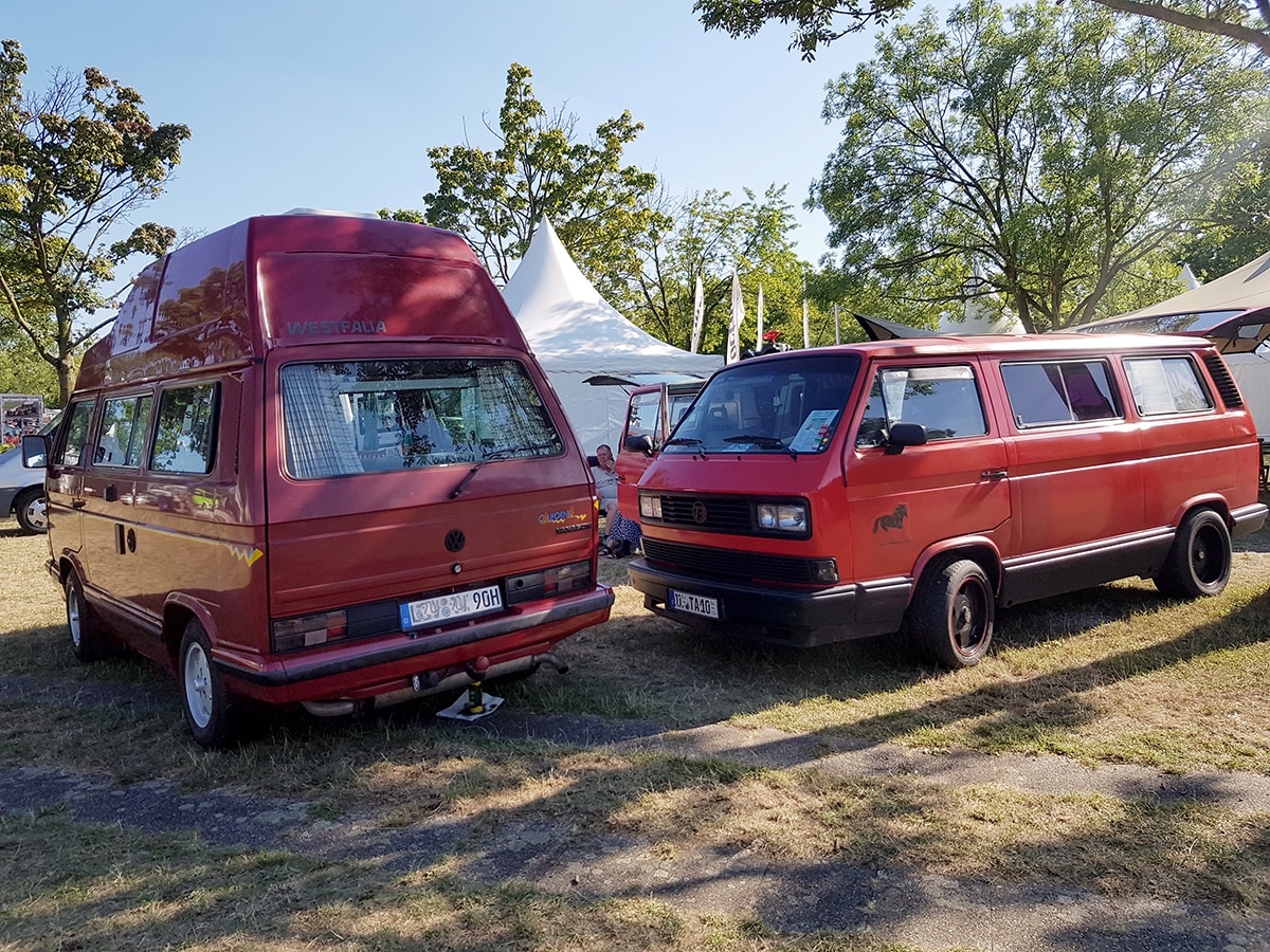 Zwei rote VW T3 Busse, einer mit Hochdach einer ohne