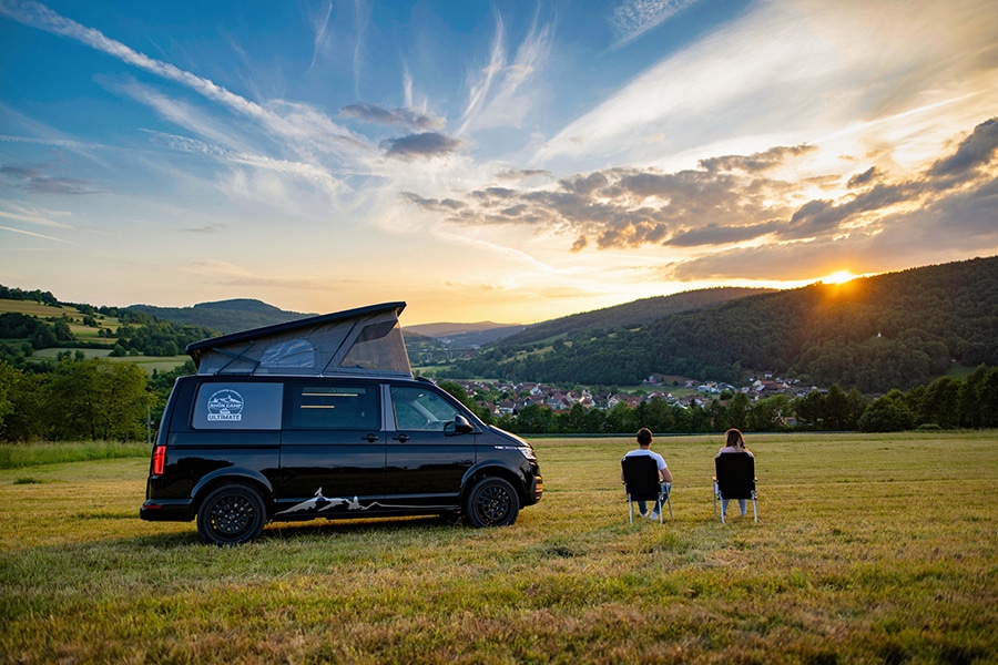 Rhön Camp Ultimate und zwei Camper auf Campingstühlen vor Abenddämmerung fotografiert