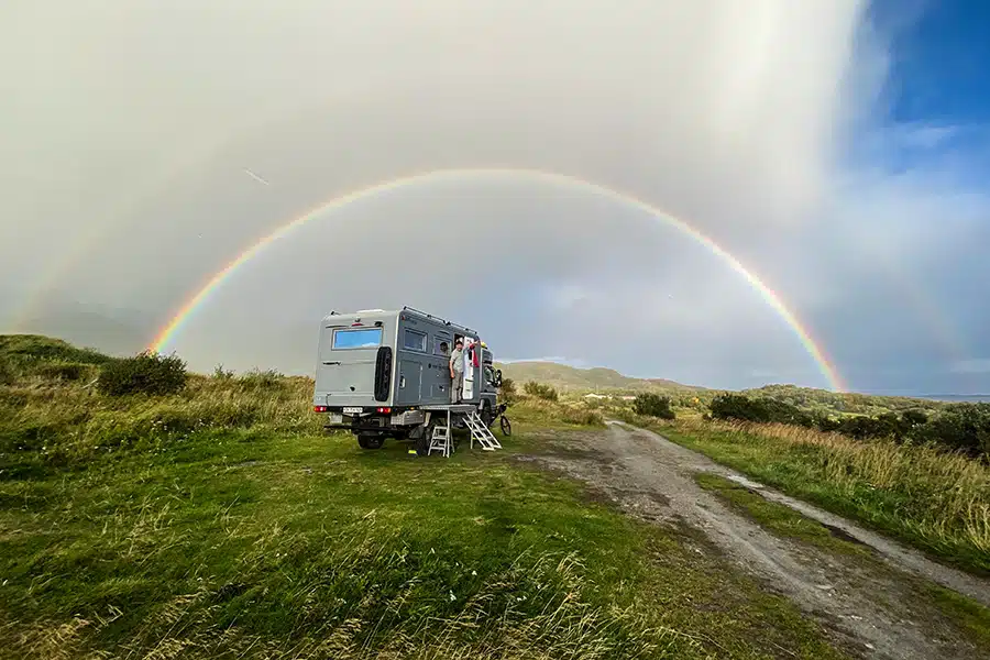 Expeditionsmobil in der grünen Landschaft Norwegens unter einem Regenbogen
