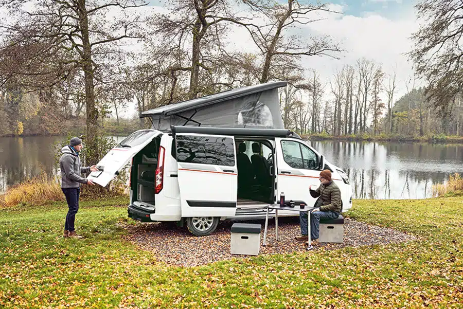 Dethleffs Globevan auf herbstlicher Wiese an einem See, vor dem Fahrzeug sitzt ein Camper und ein weiterer Camper steht an der geöffneten Heckklappe