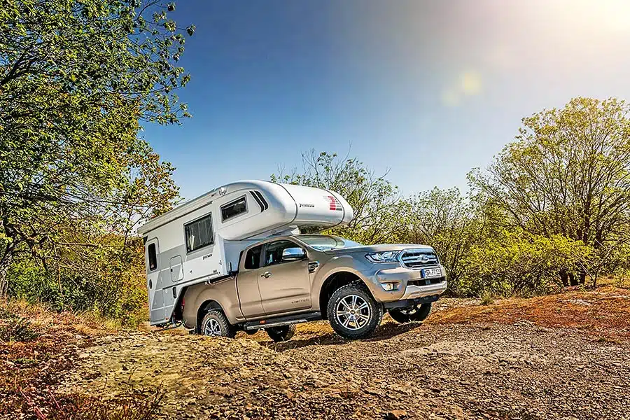 Grauer Pick-up mit weißer Alkoven-Wohnkabine offroad bergauf unterwegs