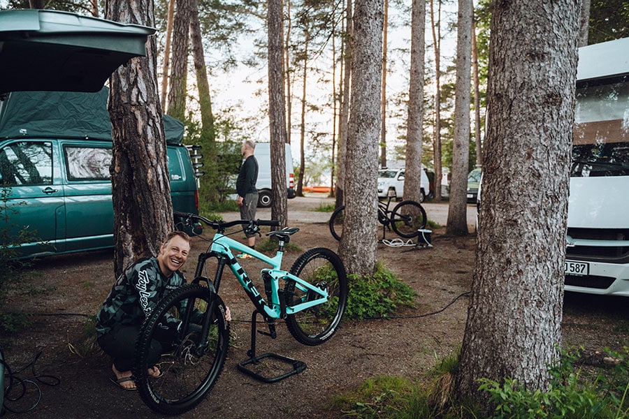Mountainbiker neben seinem Bike im Waldgelände, einige Campingfahrzeuge stehen in der Umgebung