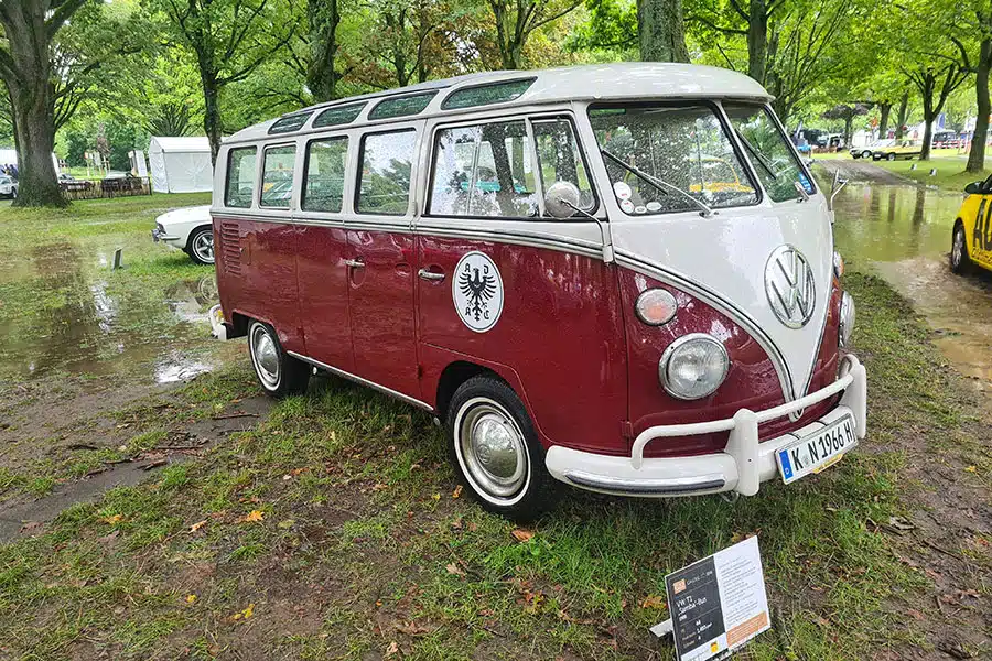 Rot-weißer VW-Bus-Oldtimer auf Parkplatz mit Baumbestand