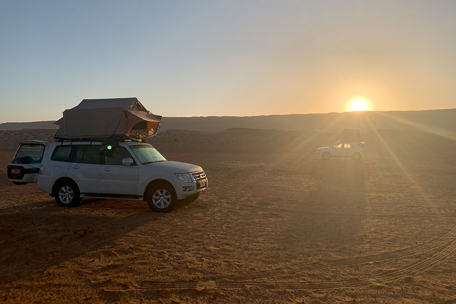 Weißer Geländewagen in der Wüste bei untergehender Sonne