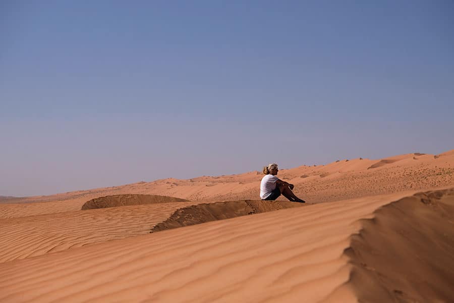 Frau sitzt inmitten der Sanddünen einer Wüste