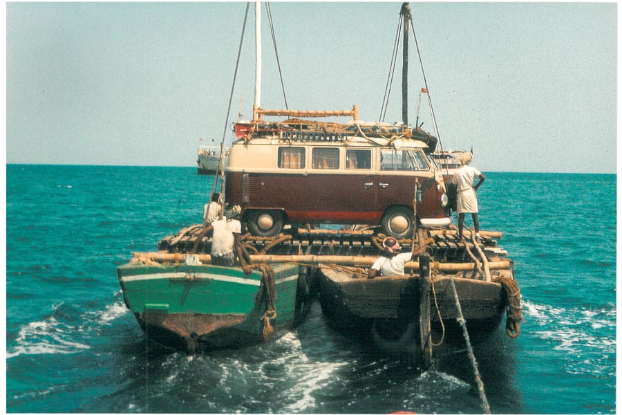 Rot-weißer VW T1 wird von zwei nebeneinander fixierten Booten übers Wasser transportiert