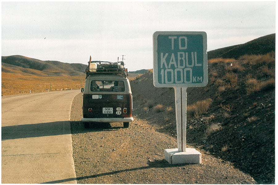 Straßenschild in karger Landschaft, dahinter parkt ein rot-weißer VW Bus