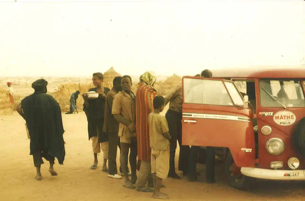 Eine Gruppe Menschen steht neben einem VW Bus in der Wüste