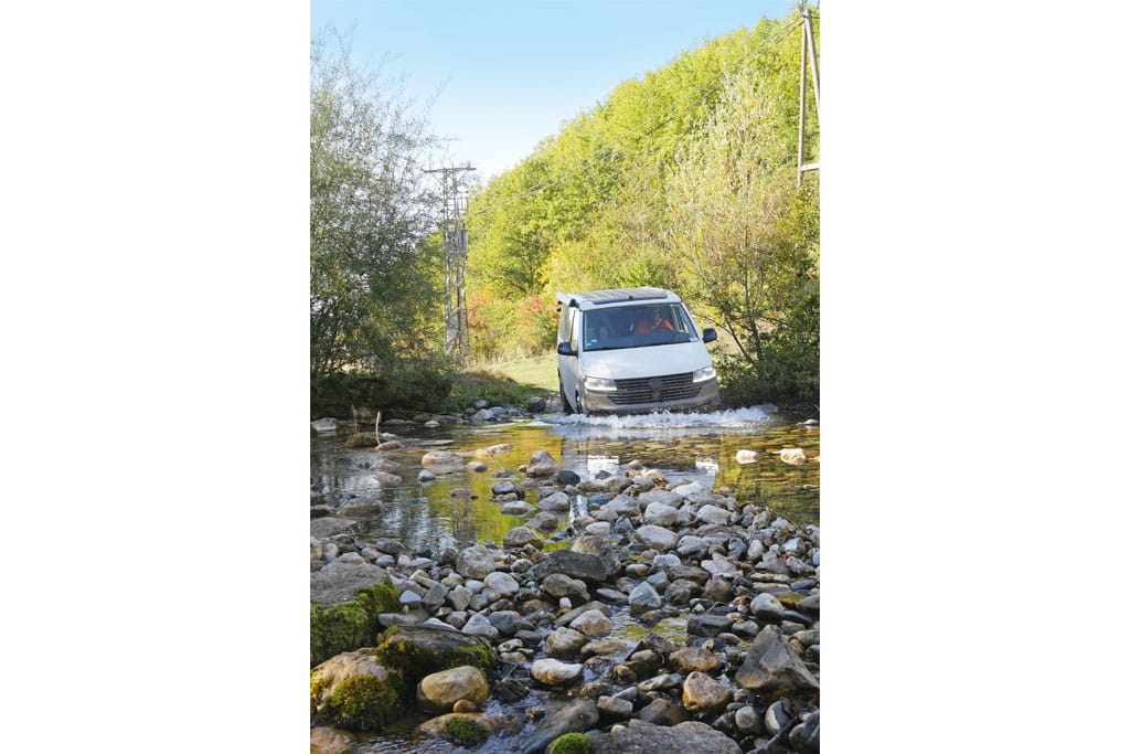 Campingbus fährt durch einen seichten Bach