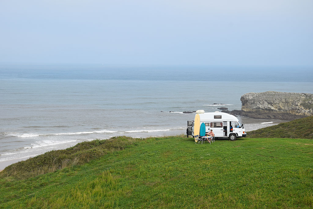 Weißer Mercedes Oldtimer Campingbus auf einer Wiese an der felsigen Meeresküste
