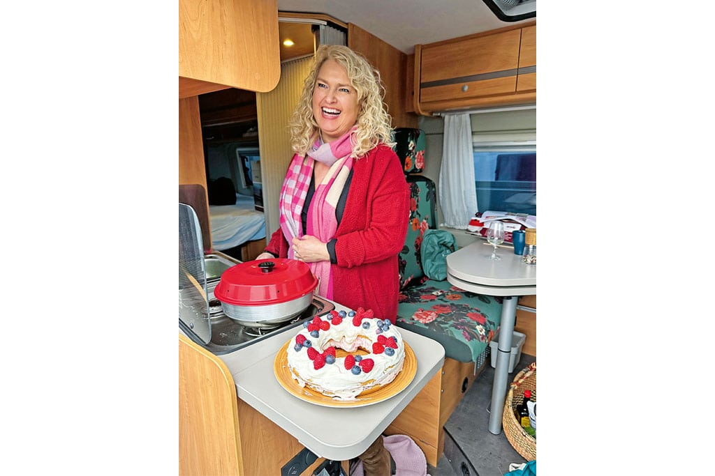 Frau steht im Camper, auf dem Küchenblock ein Omnia und ein verzierter Kuchen