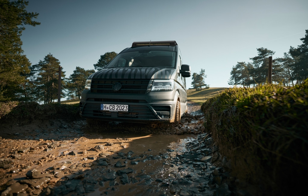 Kastenwagen fährt auf einem schlammigen Weg in einer Landschaft mit einigen Bäumen