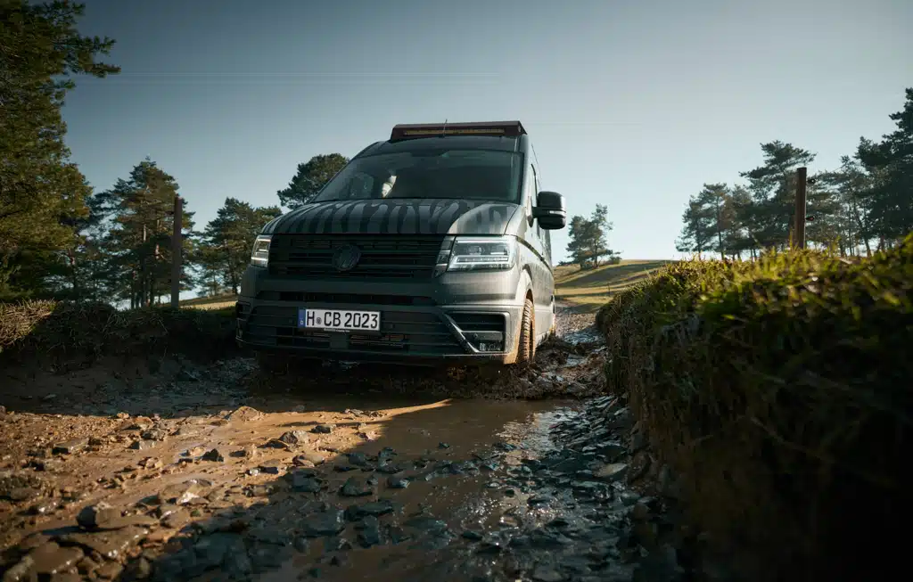 Kastenwagen fährt auf einem schlammigen Weg in einer Landschaft mit einigen Bäumen