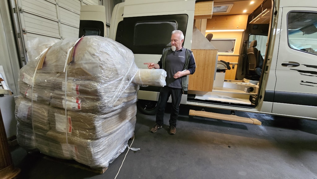Mann mit großen Packungen Dämmwolle vor dem CamperVan.