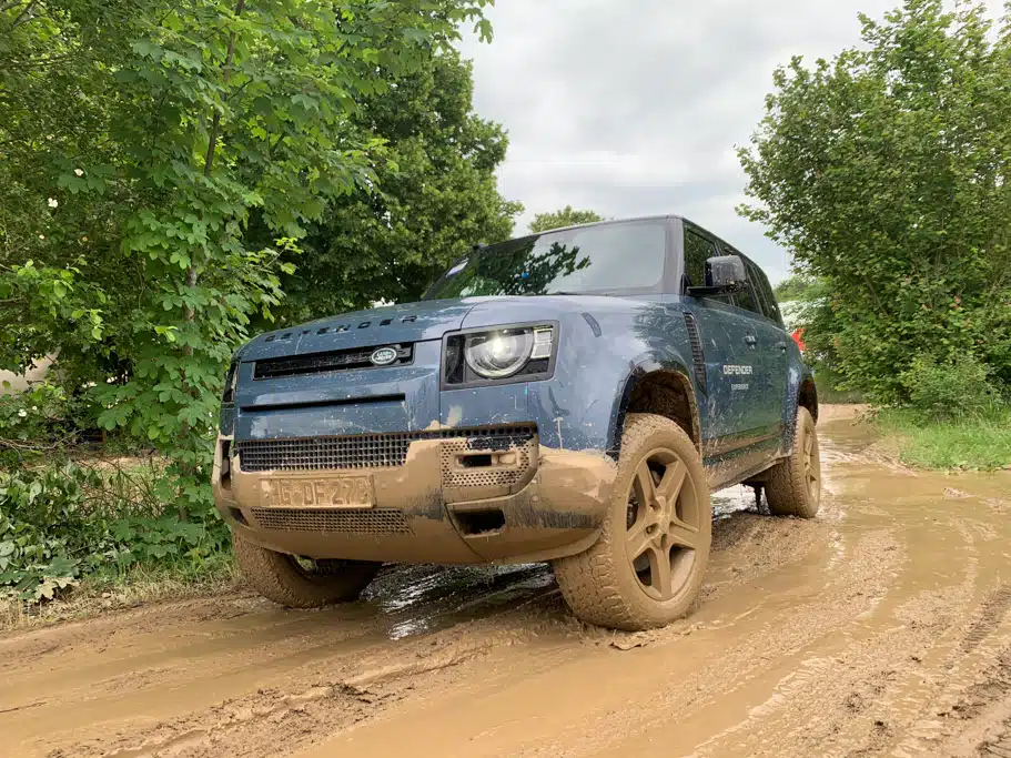 Blauer Land Rover fährt einen schlammigen Weg zwischen Bäumen entland