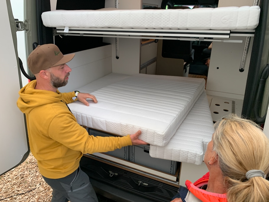 Heckgarage mit Hubbett an einem Campingfahrzeug, davor stehen eine Frau und ein Mann