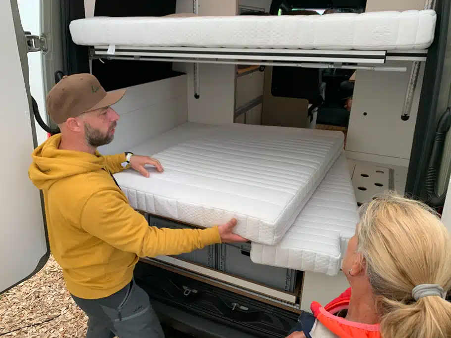 Heckgarage mit Hubbett an einem Campingfahrzeug, davor stehen eine Frau und ein Mann