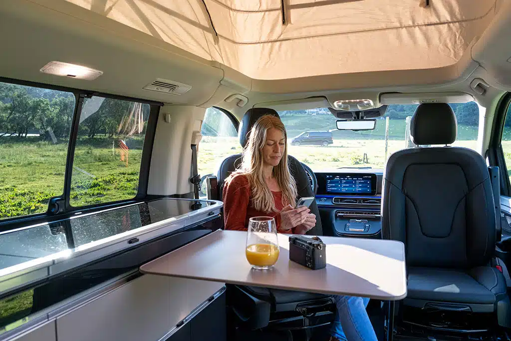Frau auf umgedrehtem Fahrersitz in einem Campervan mit aufgestelltem Dach