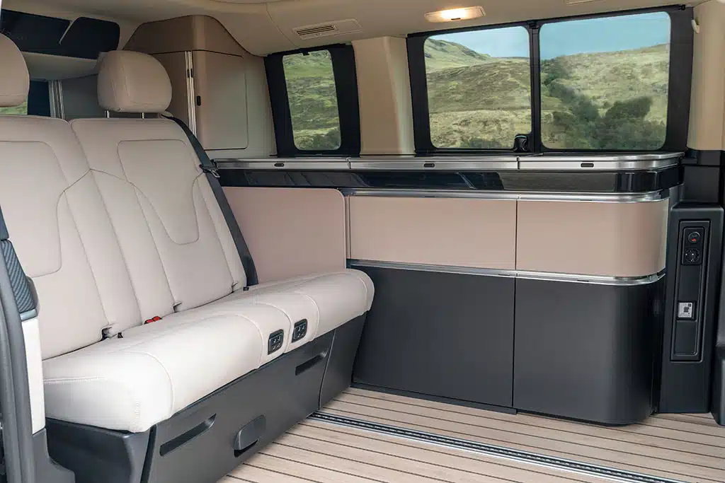 Beigefarbene und dunkelgraue Schränke und Küchenmodul im Campervan mit Rücksitzbank mit beigefarbenem Bezug