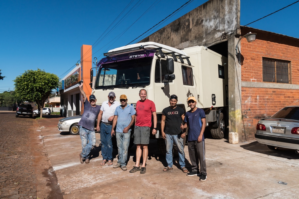 Eine Gruppe argentinischer Männer steht vor dem Fahrzeug der Familie Jöckel in einer Werkstatt