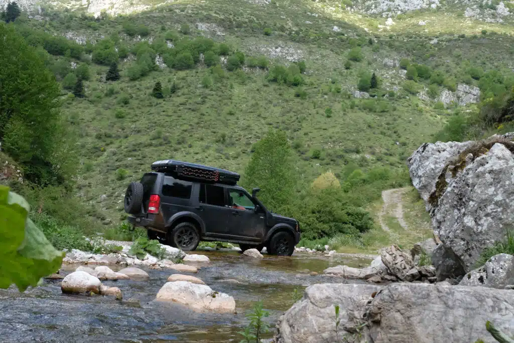 Offroad-Fahrzeug mit Dachzelt fährt durch flaches, steiniges Flussbett
