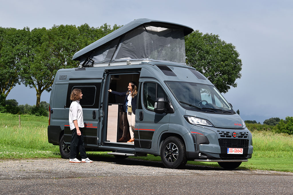 Neues Campervan-Sondermodell von Bürstner mit moderner Beklebung, lackiert in Grau, mit Aufstelldach, auf einem asphaltierten Platz neben einer Wiese mit einigen Bäumen