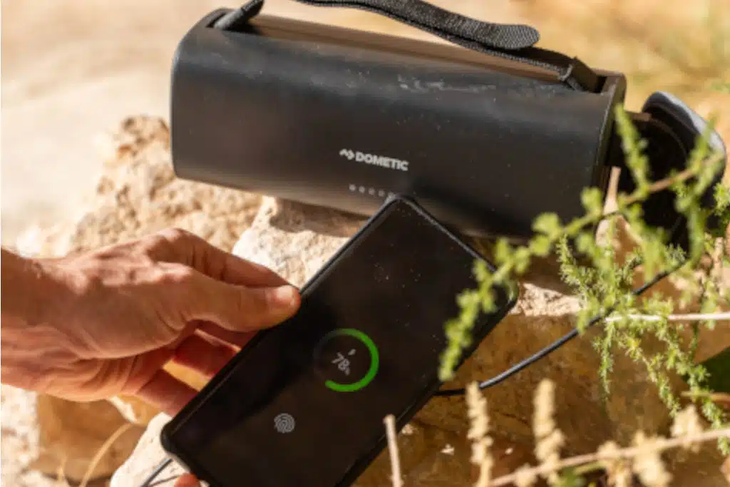 Handy ist an Powerbank angeschlossen und lädt, Powerbank liegt auf sandigem Fels