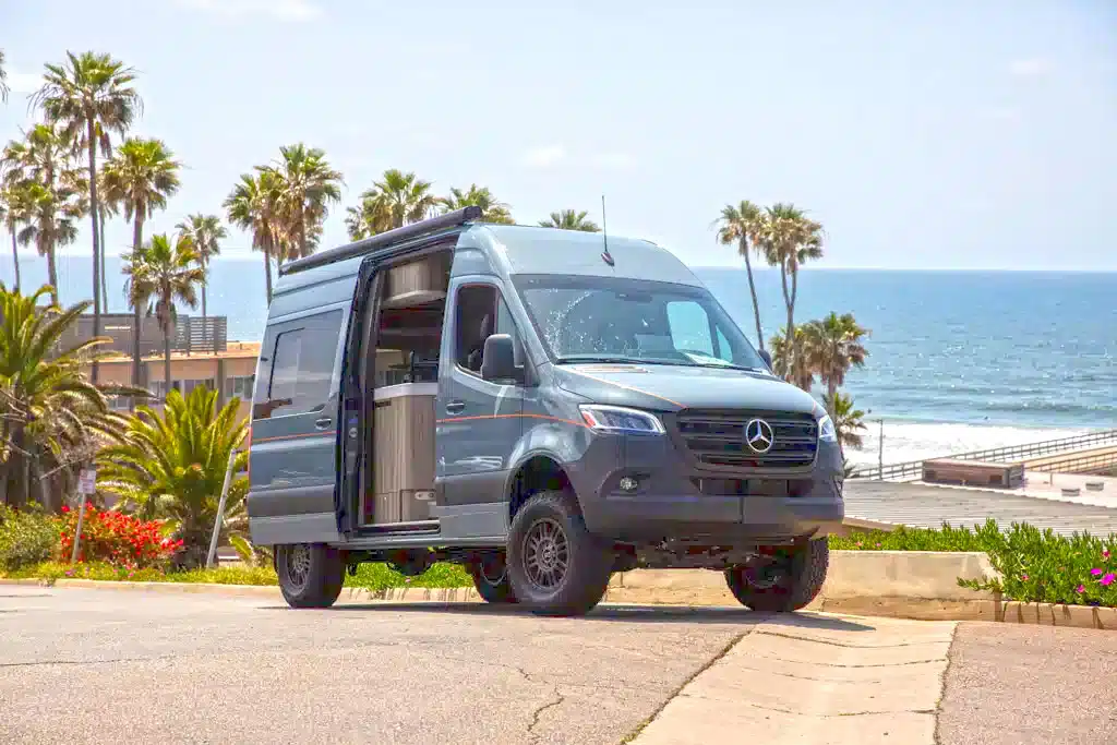 Silberner Mercedes-Sprinter-Allradvan mit Campingausrüstung am Meer