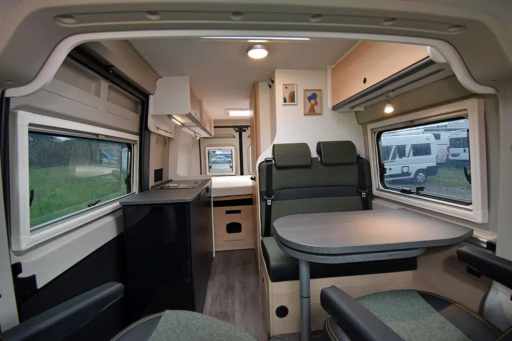 Moderner Campervan-Wohnraum mit warmen Holztönen und grünen Polstern.