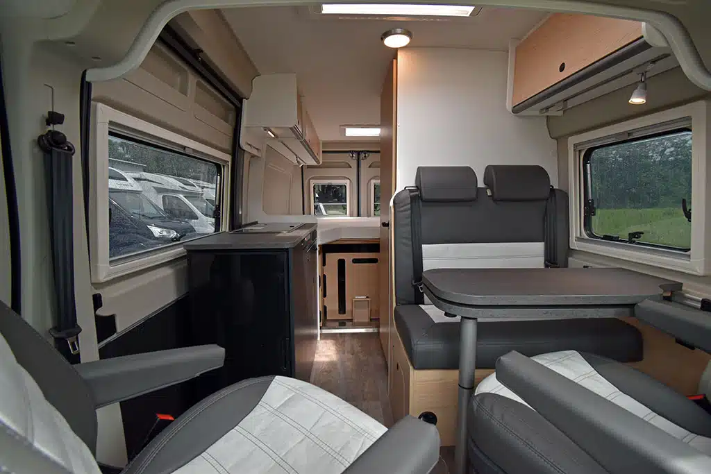 Moderner Campervan-Wohnraum mit warmen Holztönen und grauen Polstern.