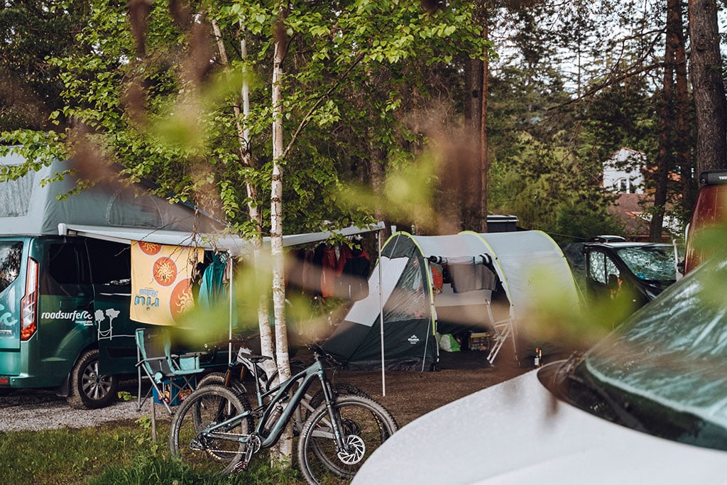 Campingbusse, ein Zelt und ein Mountainbike in einem Waldstück