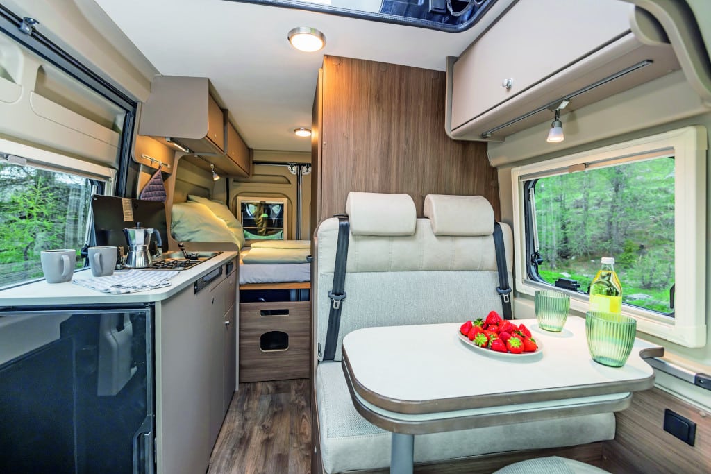 Durchsicht nach hinten mit heller Sitzgruppe und hellem Küchenblock gegenüber vor hellbrauner Möblierung