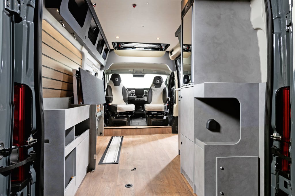 Durchsicht nach vorne. Links eine ausklappbare Längs-Couch, rechts der Küchenblock mit oben eingesetztem Kühlschrank.