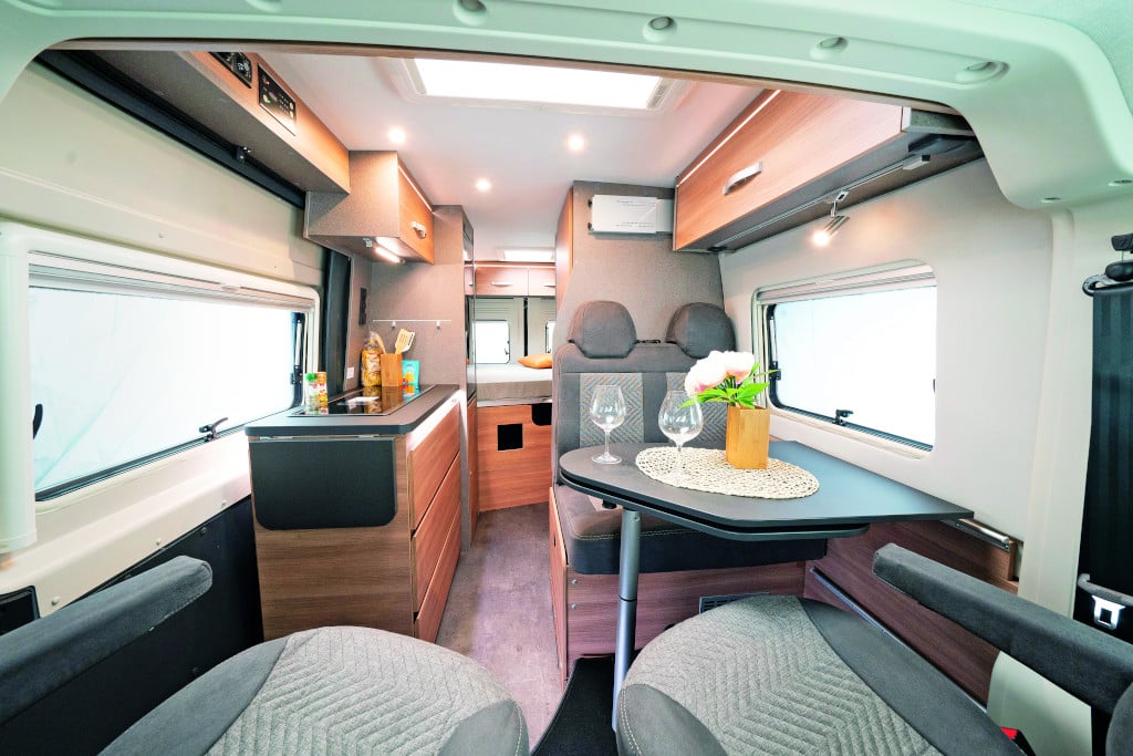 Durchsicht nach hinten auf Sitzgruppe mit gedrehten Vordersitzen, Küchenblocl links und Querbett im Heck