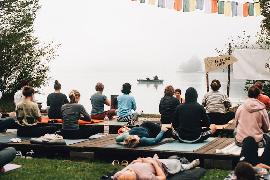 Eine Gruppe Menschen macht Yoga auf Holzplattformen am Seeufer