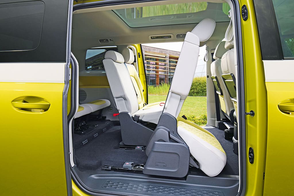 Blick durch die offene Schiebetür eines gelb.weißen ID. Buzz auf die mittlere Sitzreihe, deren vorderster der drei Einzelsitze nach vorne gekippt ist