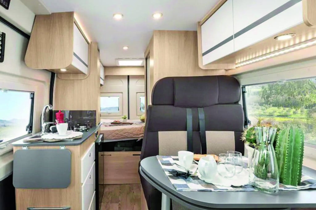 Durchblick nach hinten, Sitzgruppe mit dunklem Polster, hellem Tisch und hellen Möbeln mit Querbett im Heck