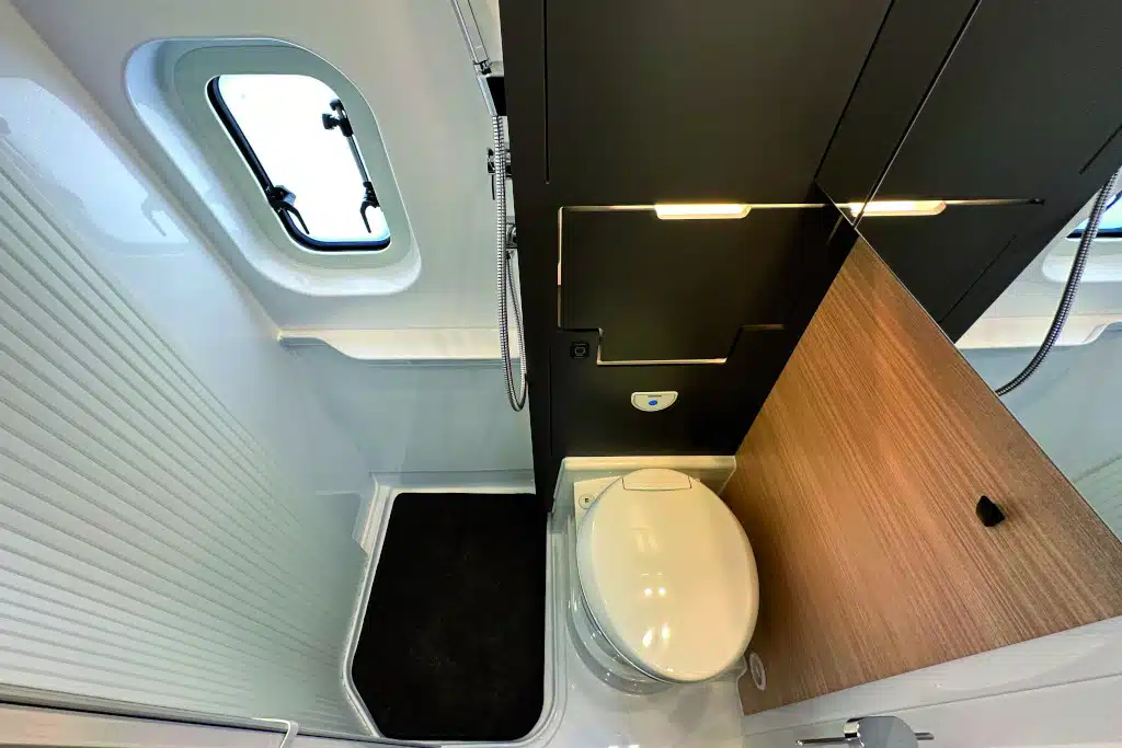 Blick ins Bad von erhöhter Position. Links Dusche, rechts davon abtrennbar Toilette mit engeklapptem Waschbecken