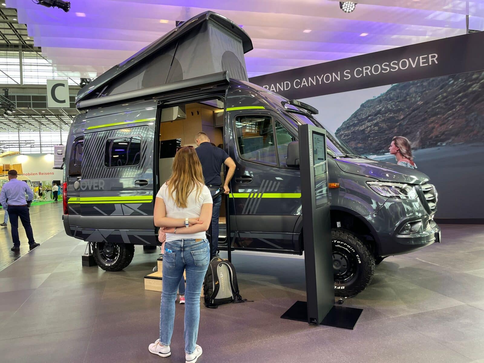 Dunkelgrauer Offroad-Campervan in einer Messehalle mit Besuchern