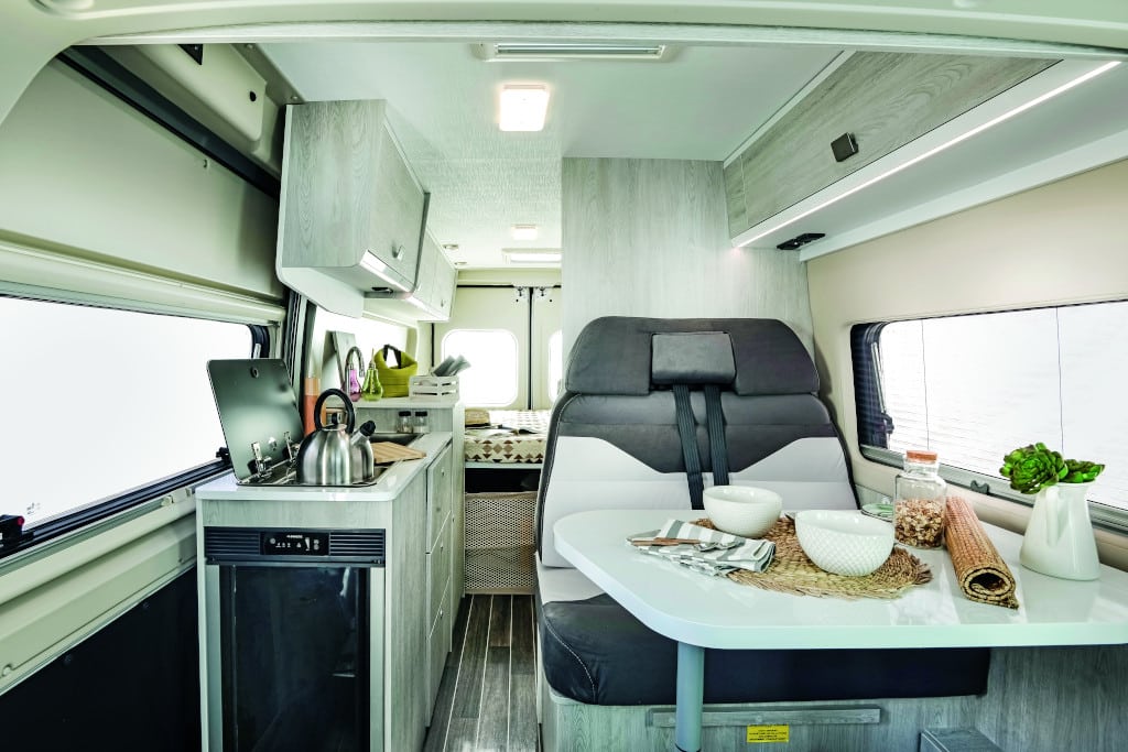 Blick auf Sitzgruppe: Helle Möblierung, dunkle Polster, Querbett im Heck