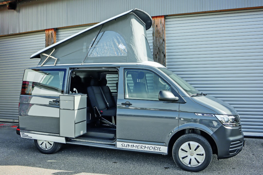 Fahrzeug von außen mit aufgestelltem Dach, geöffneter Schiebetüre und ausgeschwenktem Küchenblock