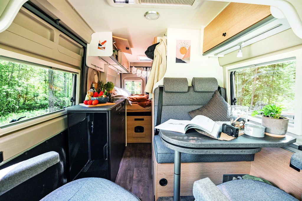 Hellgraue Zweier-Sitzbank und Tisch gegenüber Möbel in hellem Dekor und Küchenblock in Schwarz.