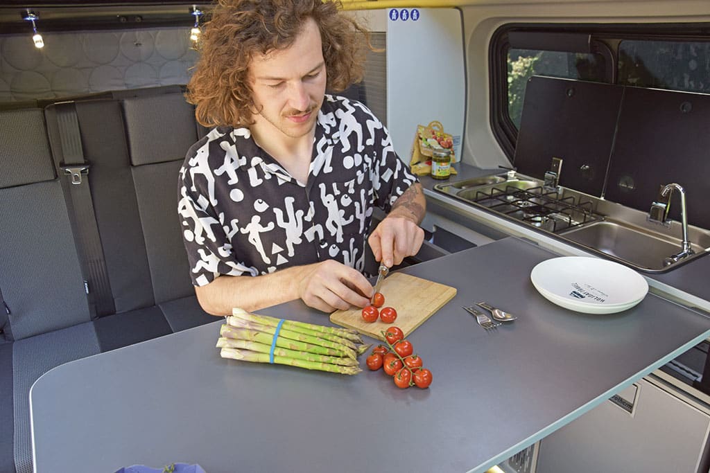 Mann schneidet Gemüse am Tisch im Campingbus