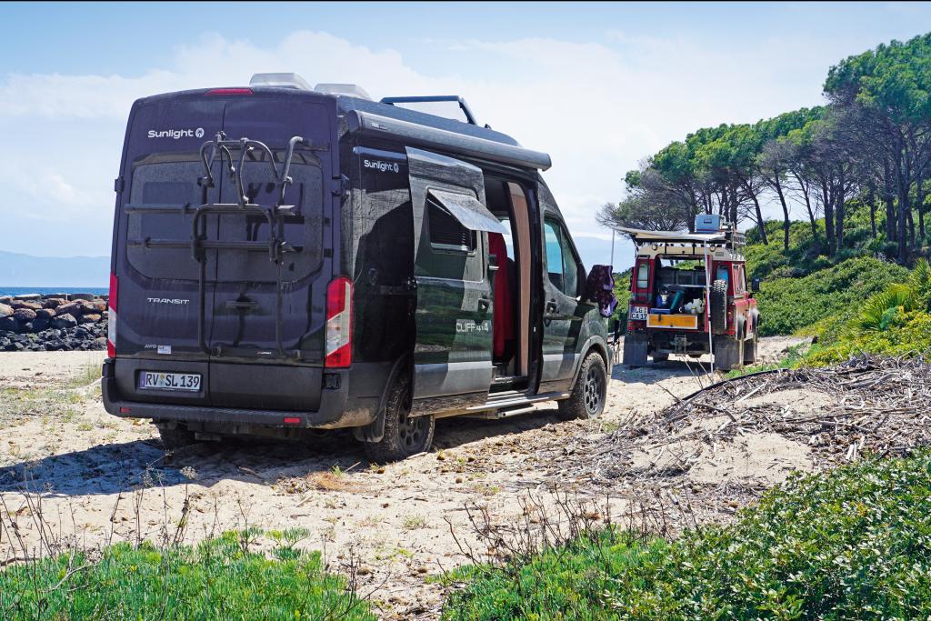 Schwarzer Campervan parkt vor einem roten Geländewagen