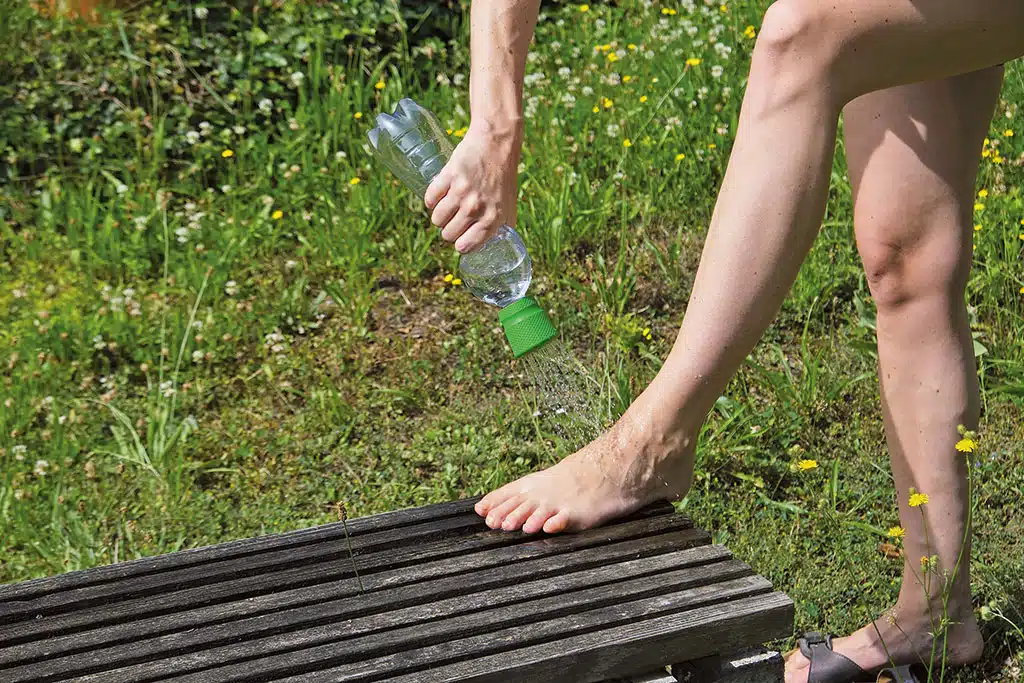 Eine Person nutzt eine Wasserflasche mit aufgesetztem Duschkopf fürs Füße waschen