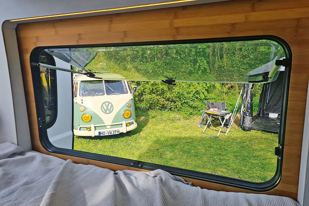 Ausstellfenster im Campervan, draußen vor dem Fester steht ein türkis-weißer VW-Oldtimer-Bus